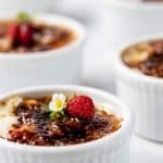 close up photo of a strawberry blossom garnished strawberries and cream dessert in a ramekin