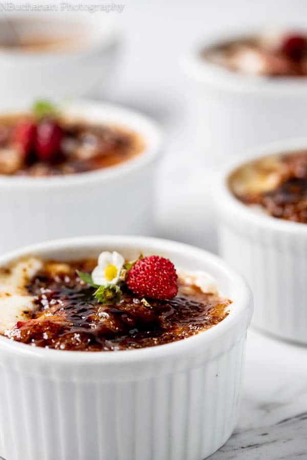 close up photo of a strawberry blossom garnished strawberries and cream dessert in a ramekin