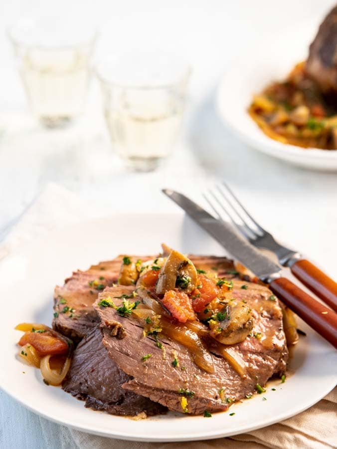 plate with top round roast and sauce with wine in the background.