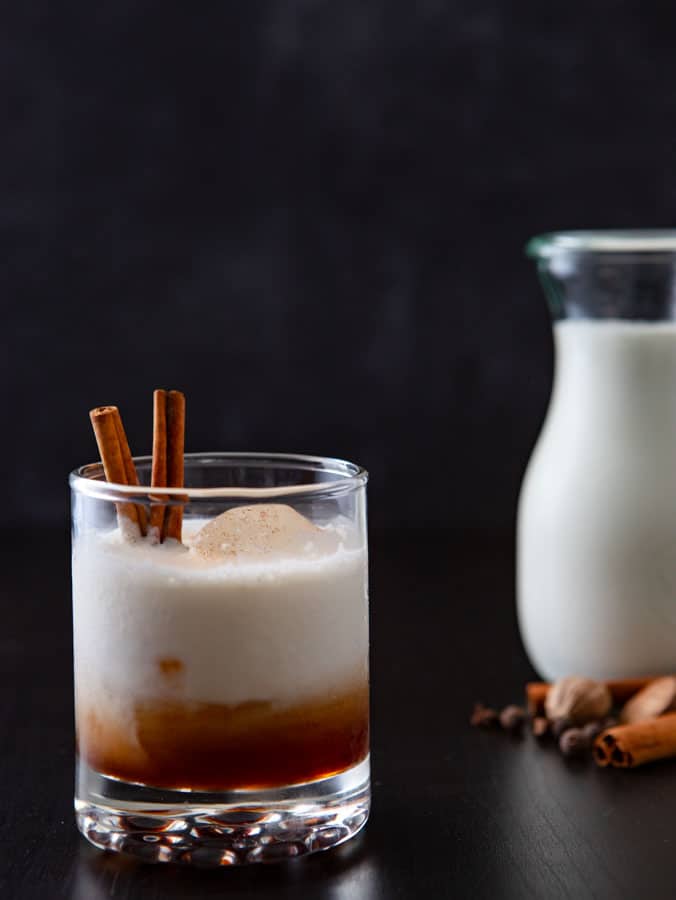 Glass of spiced infused white russian drink with milk and spices in the background.

