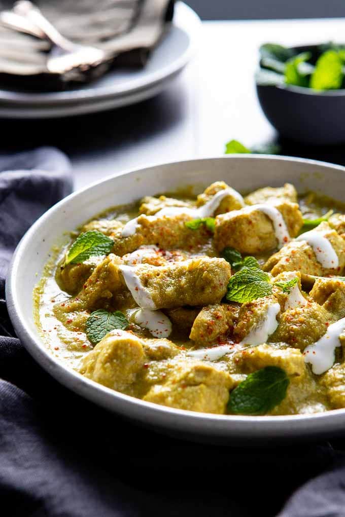 Bowl of chicken Korma with plates and garnishes in the background