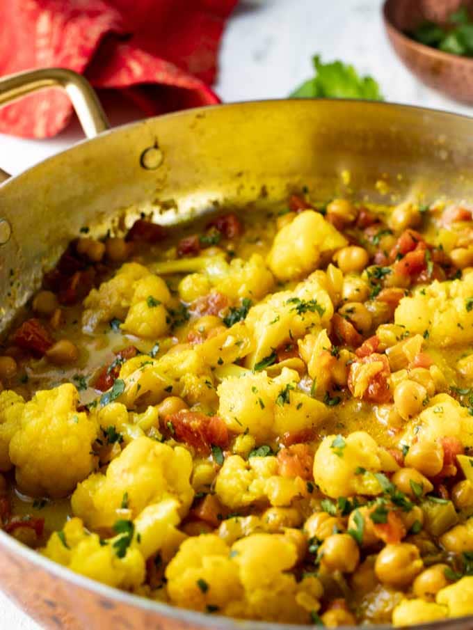 Skillet with Cauliflower Chickpea Curry made with coconut and garnished with minced cilantro.
