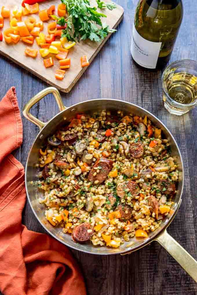 Overhead image of barley risotto with italian sausage and peppers with a glass of wine.