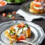A single aloo tikki on a plate garnished with yogurt, chutney tomato and onion.