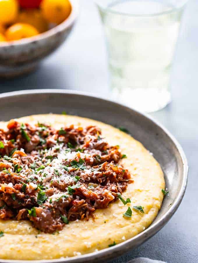 Bowl of italian ragu over polenta garnished with parsley and grated parmesan cheese.
