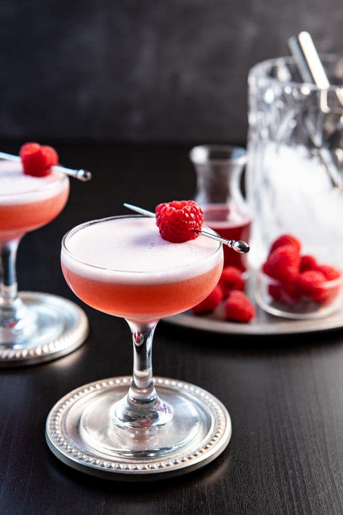 A coupe glass with the Clover Club Cocktail garnished with a single raspberry.
