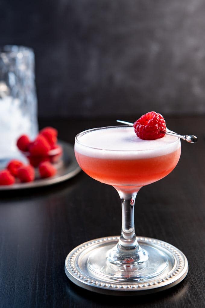 A glass of the clover club cocktail recipe with a raspberry garnish. 