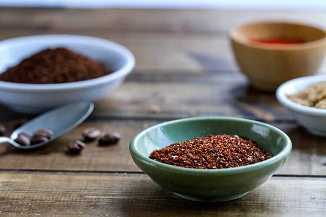 Coffee and spice rub in a bowl with ground coffee and spices in the background.