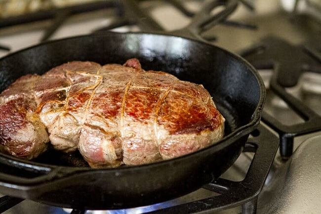 sirloin roast being seared in a skillet on the stove.