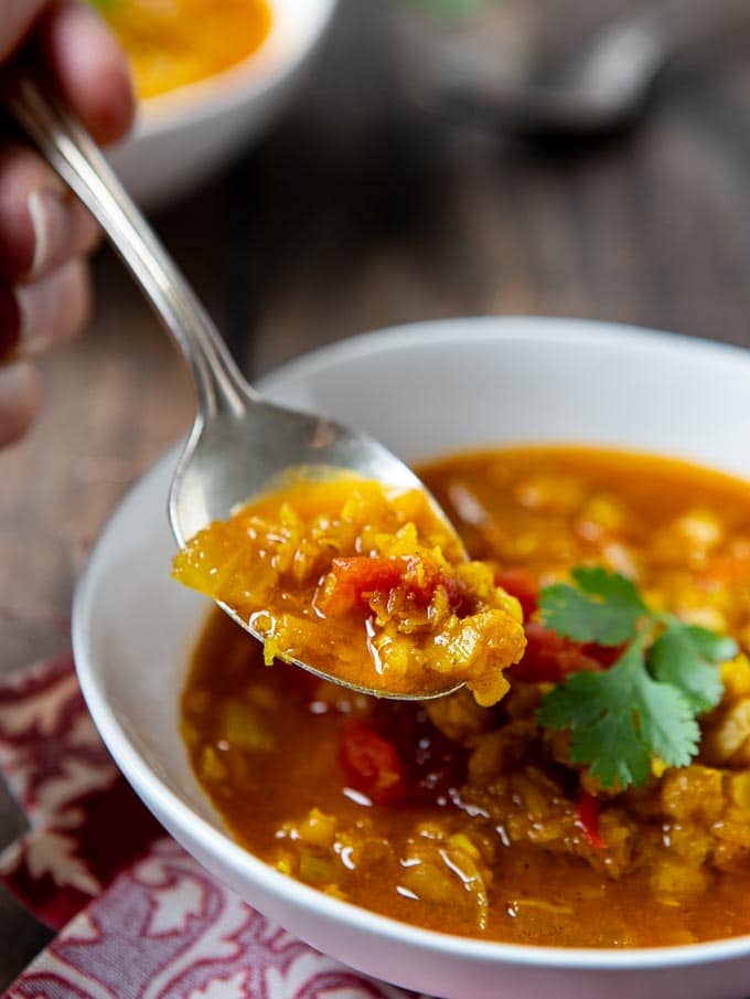 bowl of spicy lentil soup with a spoon scooping up a portion. 