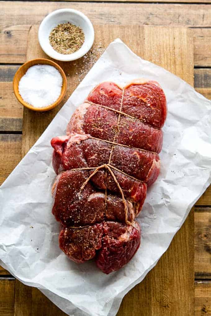 Sirloin roast tied with butcher's twine on a cutting board and seasoned with salt and pepper.