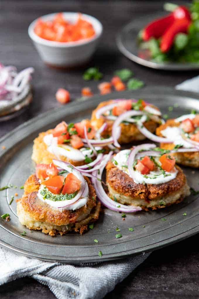 Aloo tikki or Indian Potato patties on a platter, garnished with tomatoes, onions, yogurt and chutney.
