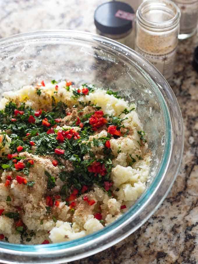 clear bowl with mashed potatoes, spices, chiles and cilantro for making aloo tikki.