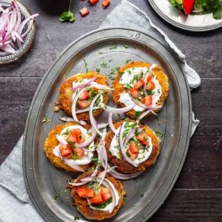 Aloo tikki's on a metal platter and garnished with tomatoes, onions, yogurt, mint chutney and cilantro.