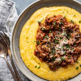 Shredded pork ragu on instant pot polenta in a bowl with a napkin and silverware