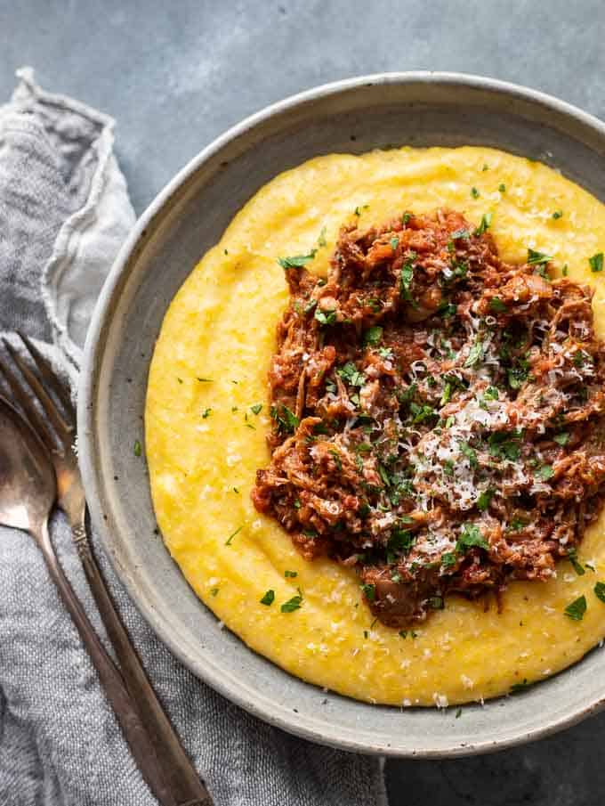 Overhead photo of an easy pork ragu recipe
 on top of polenta in a bowl with silverware and a napkin.
