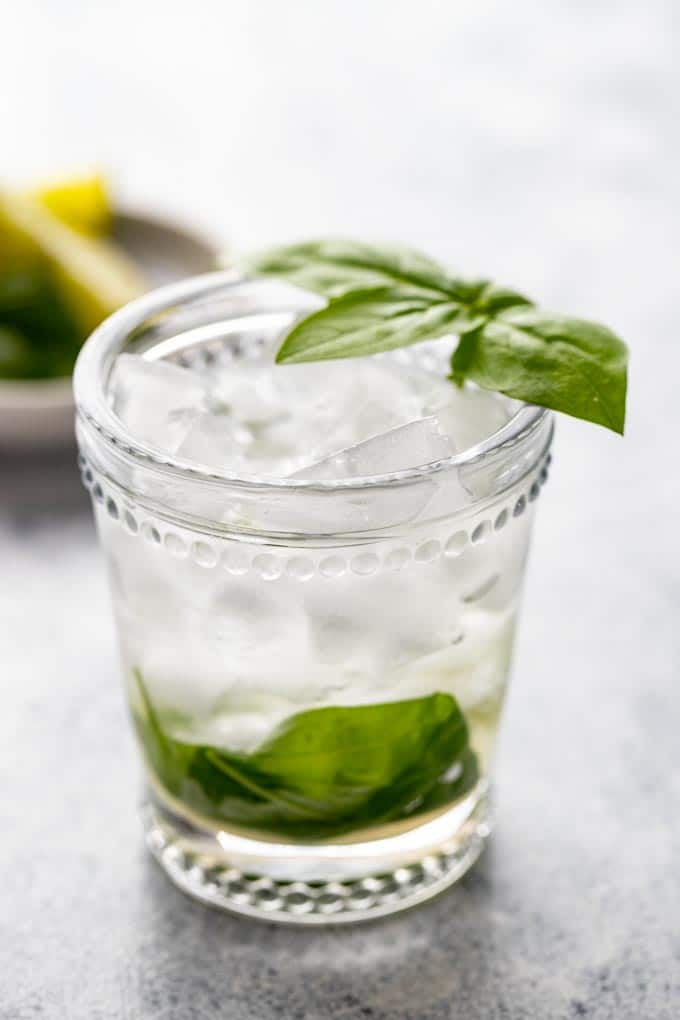 Single glass of vermouth on the rocks with a basil leaf garnish.
