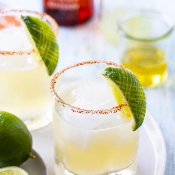 Two margaritas on the rocks with a lime garnish on a white platter.