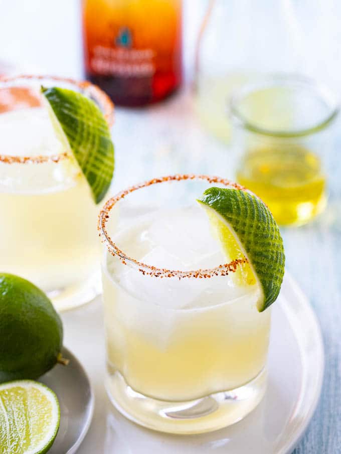 Platter with two margaritas on the rocks with limes and a bottle of tequila in the background. 
