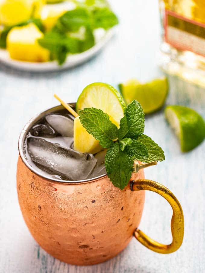 Mexican Mule in a copper mug with a bottle of tequila in the background with a plate of garnishes. 
