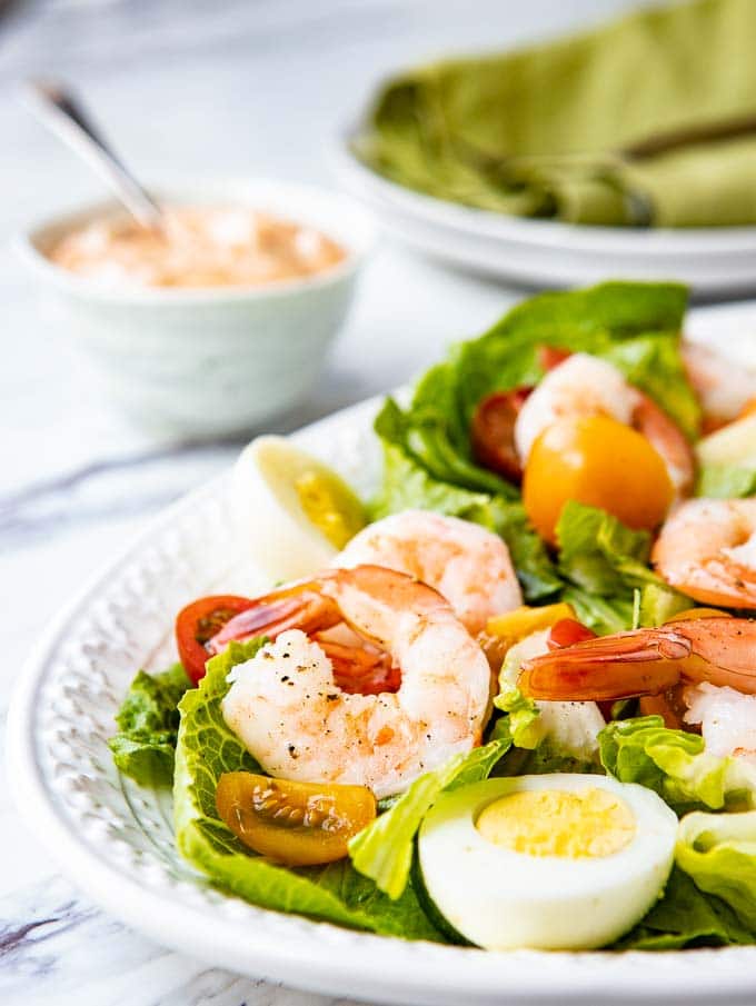 Angled shot of Shrimp Louie Salad on a platter with a bowl of louie dressing on the side.