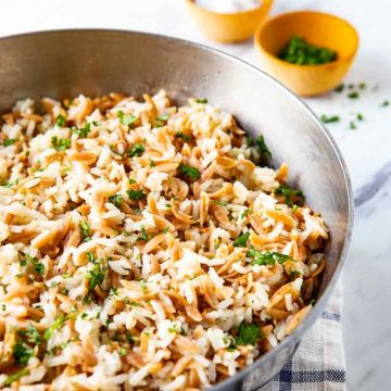 Saucepan with Rice Pilaf with orzo and small bowls of salt and parsley in the background.