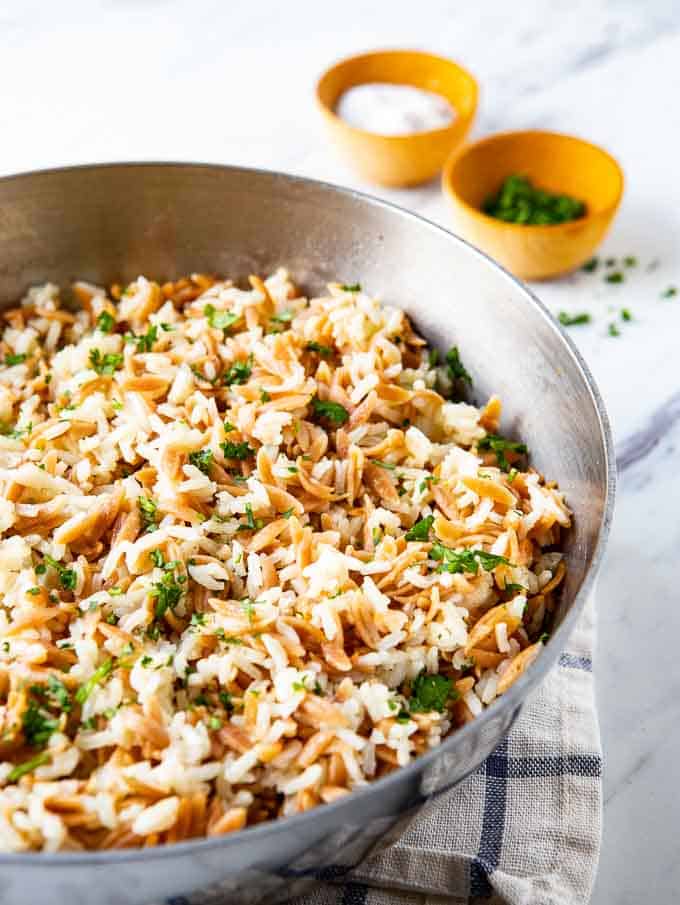 Saucepan with Rice Pilaf with orzo on a tables with parsley and salt containers in the background.
