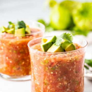 two glasses of an easy gazpacho recipe garnished with avocado and cilantro.