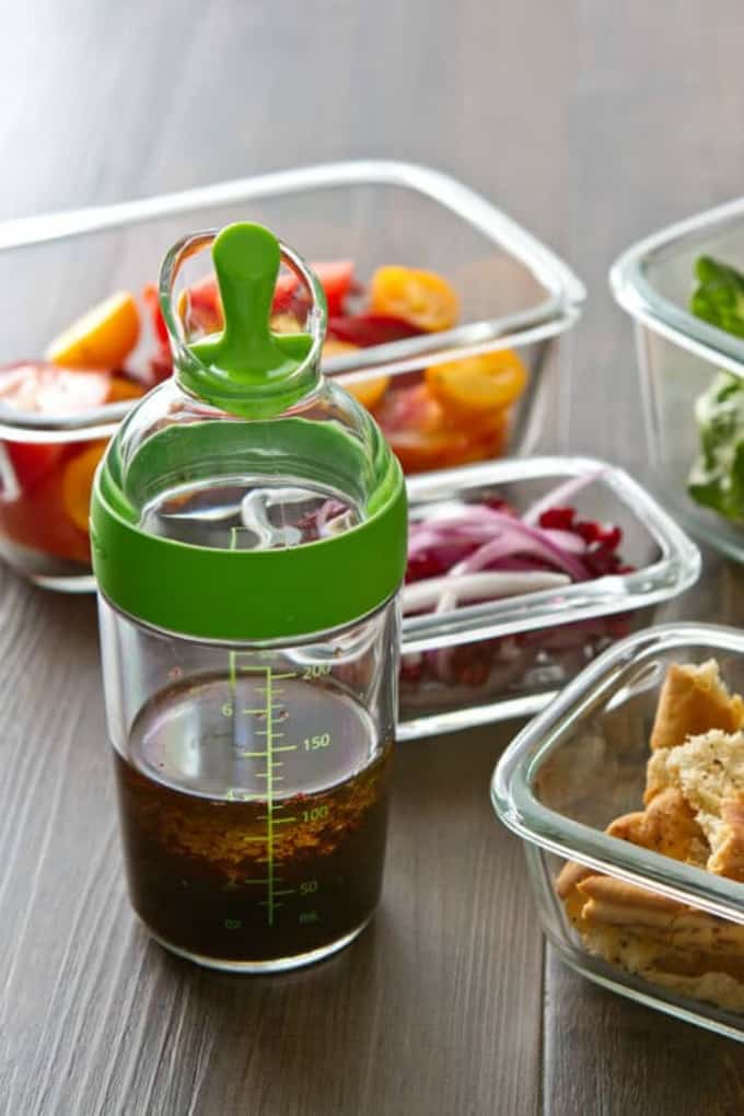 Container with Pomegranate dressing and containers of lebanese salad in the background. 