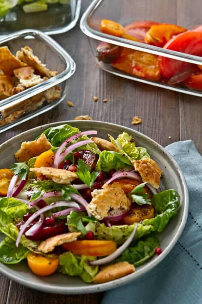 Fattoush salad in a bowl with fattoush salad ingredients in containers in the background.