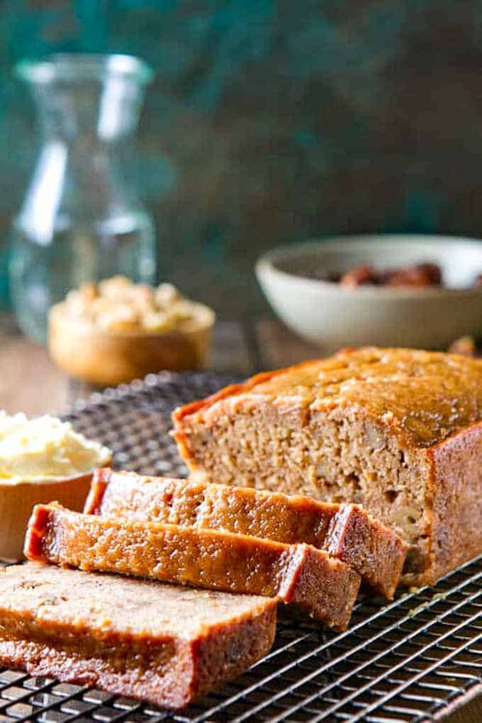 Date Nut Loaf recipe on a cooling rack with several cut slices next to a pot of butter. 