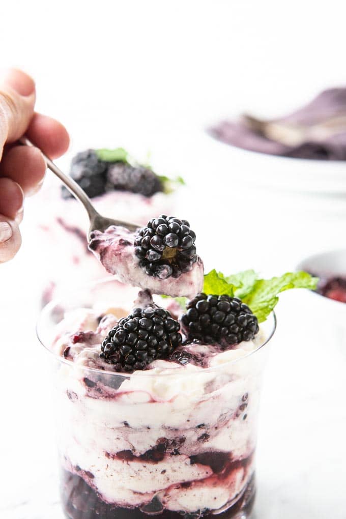 A glass filled with a traditional blackberry fool with a spoonful taking out of it. 