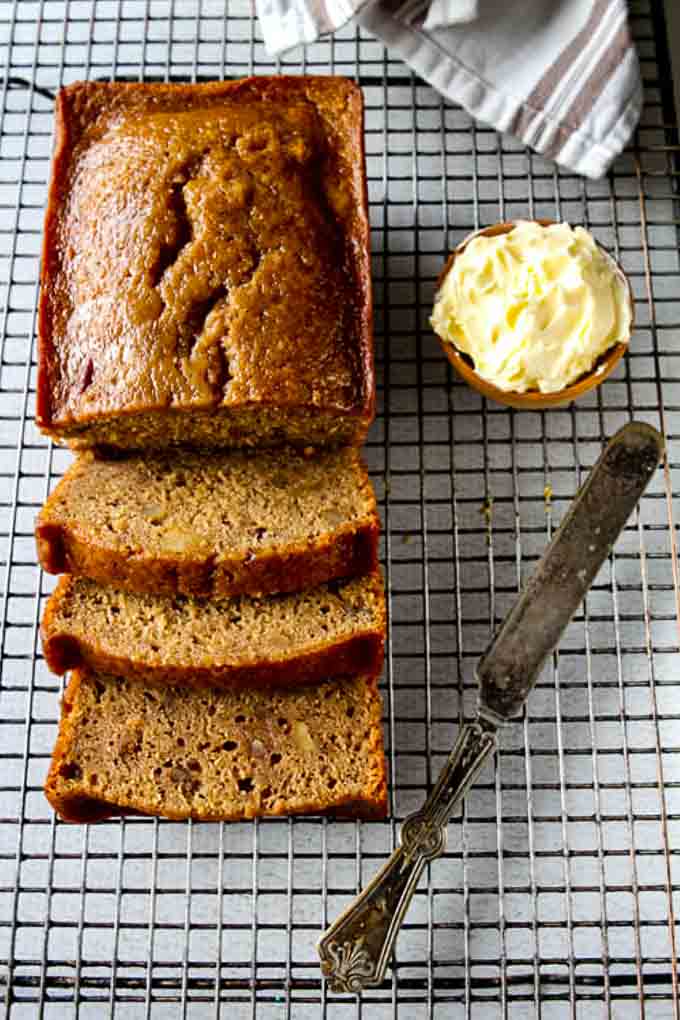 Loaf of sliced date nut bread on a cooling rack with a knife and pot of butter.