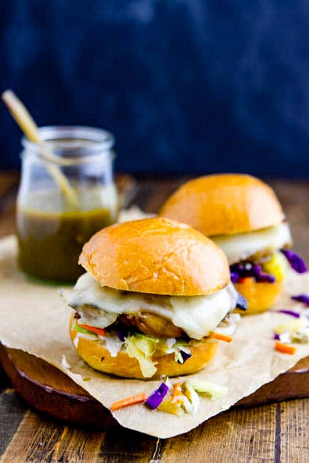 Two Chicken Sliders on a board with green chile sauce in the background. 