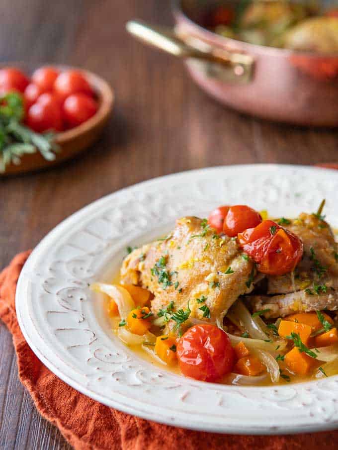 A plate showing a close up of this Chicken Contadina recipe with tomatoes and herbs in the background. 
