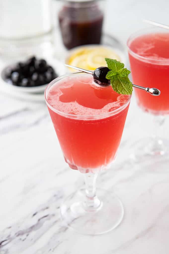 Close up of the Cherry Vodka Sour Recipe in a cocktail glass garnished with a cherry and mint. 
