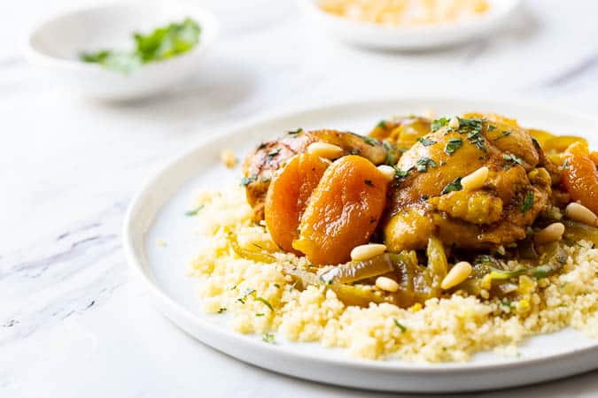 Close up photo of this Moroccan Chicken stew recipe on a plate with plain couscous underneath. 
