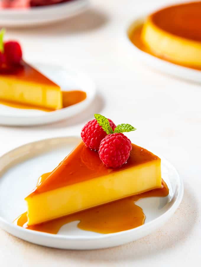 A slice of Mexican Flan on a plate with fresh raspberries and mint garnish.
