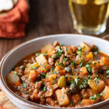 close up of a bowl with beef picadillo with tortillas in the backgrounds.