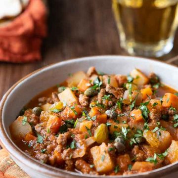 close up of a bowl with beef picadillo with tortillas in the backgrounds.