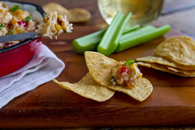 Scoop of the hot corn dip on a tortilla chip with celery in the background. 
