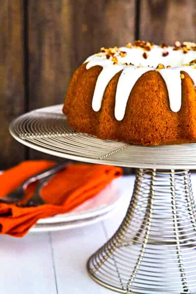 Bourbon Pumpkin bundt cake on a cake stand with plates in the background.