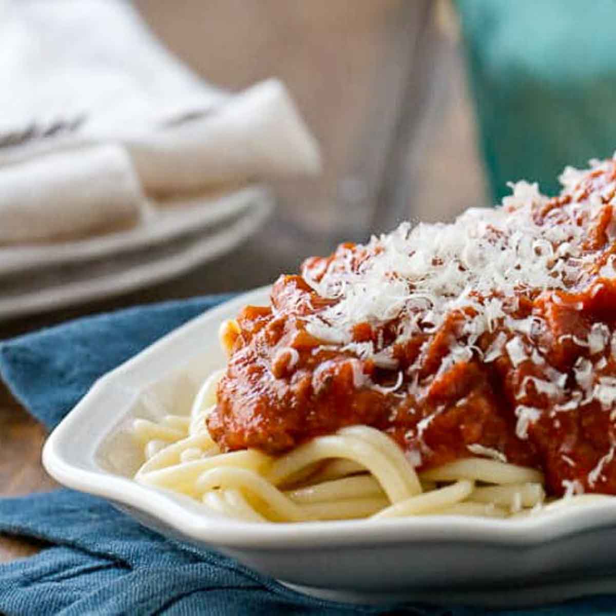 Platter of homemade spaghetti meat sauce with plates and napkins in the background.