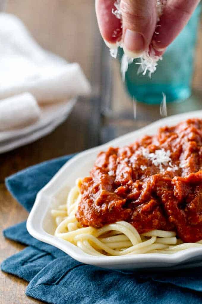 Sprinkling cheese on a platter of homemade spaghetti sauce with spaghetti noodles.
