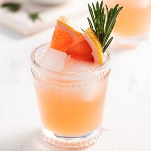 gin and elderflower cocktail in a rocks glass with a grapefruit and rosemary garnish.