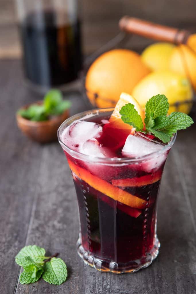 A glass of tinto  de Verano or red wine spritzer on a table with oranges, lemons and mint.