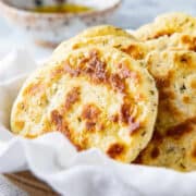 Basket with yogurt flatbreads and a bowl of olive oil in the background.