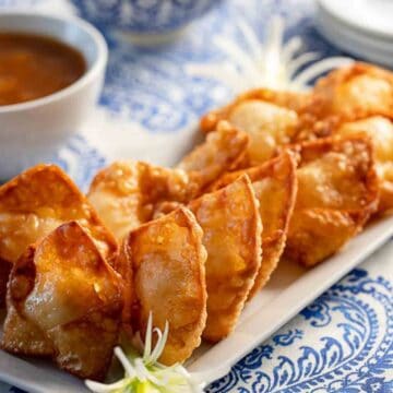 Crab Rangoon on a platter with dipping sauce in the background.