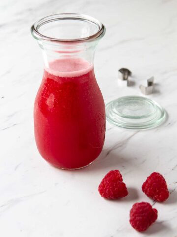 Glass jar filled with raspberry syrup.