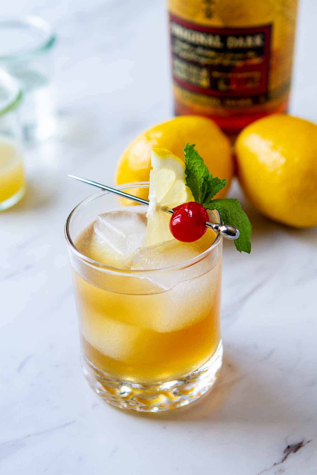 Glass of rum sour cocktail with lemons in the background.